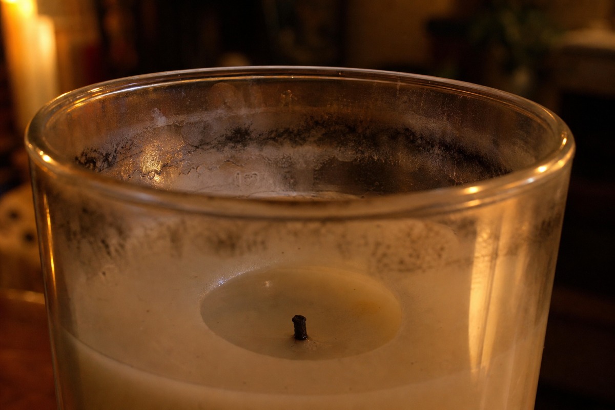 Paroi intérieure d'une bougie en verre avec des traînées noires et grasses de suie dans le tiers supérieur