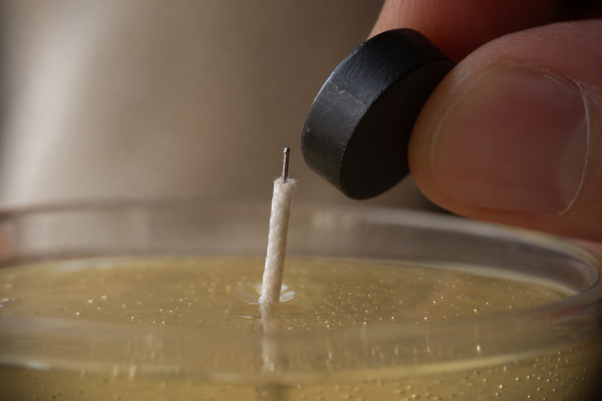 Gros plan d'une mèche extraite avec une fine armature métallique et un petit aimant approché de l'âme métallique de la mèche