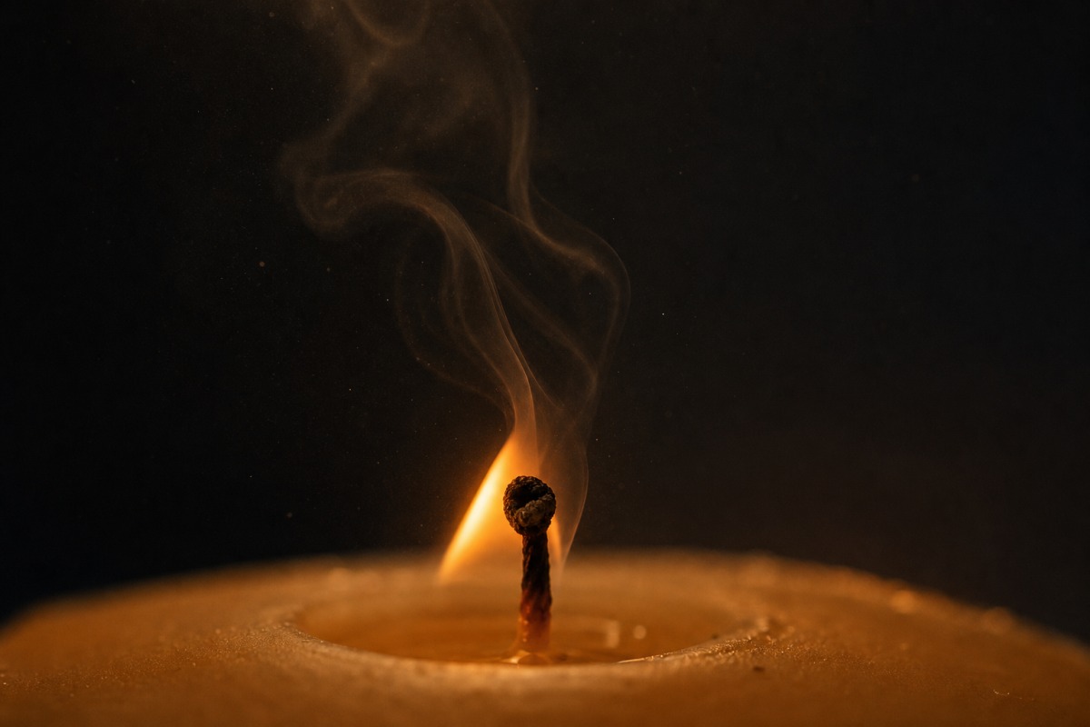 Mèche de bougie à la flamme instable et au filet de fumée noire qui s'élève dans une pièce sombre